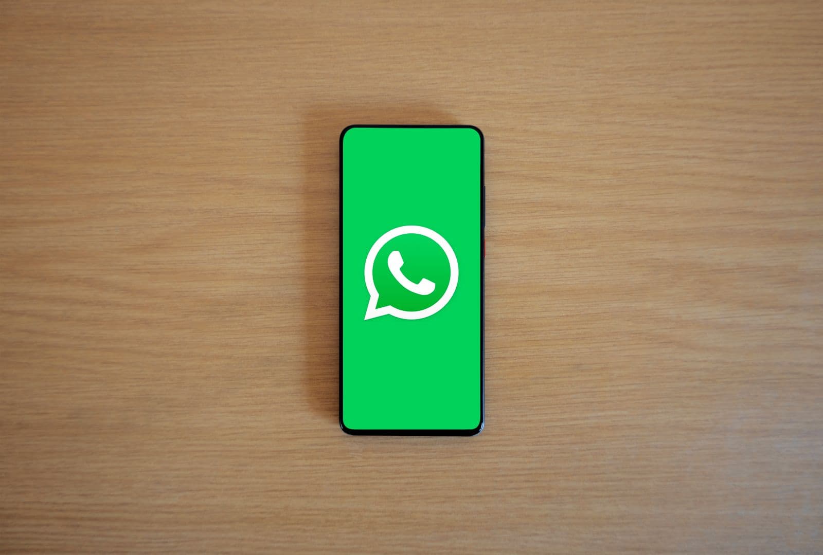 Smartphone on a wooden desk showing the WhatsApp messaging app